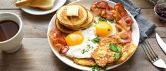 a plate with eggs, bacon and pancakes on it next to a cup of coffee