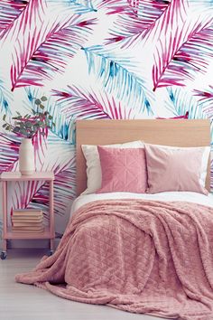 a bed with pink and blue leaves on the wall next to a night stand that has two nightstands in front of it