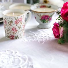 pink roses are sitting on a table next to two cups and saucers with tea in them