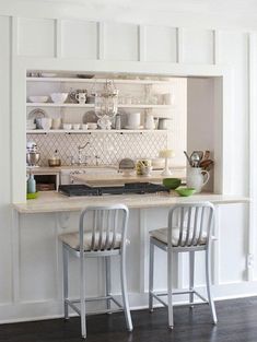 two chairs are sitting at the counter in this white kitchen with open shelving on the wall