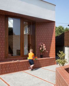 a small child is walking up the side of a brick building with flowers in front of it