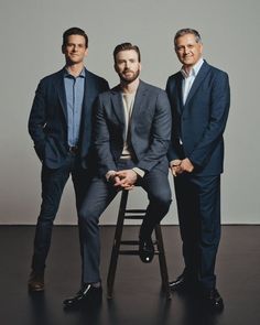 three men in suits are sitting on a stool and posing for the camera with one man wearing a suit