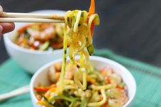 someone is holding chopsticks over a bowl of food with vegetables and noodles in it