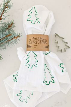 four white napkins with green christmas trees on them and a brown tag that says merry christmas