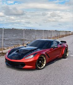 a red and black sports car parked on the side of the road next to a body of water