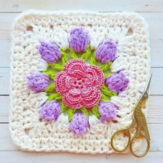 a crocheted square with pink and purple flowers on it, next to a pair of scissors