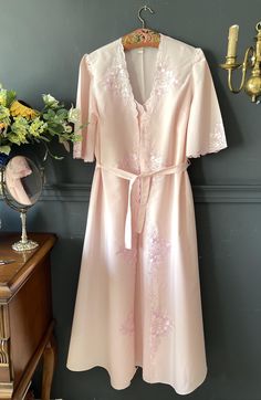 This unique set, specially designed in the 1950s, consists of a Robe and Nightgown, bringing together nostalgia and elegance. This magnificent set is made of light pink cotton Poplin Fabric, allowing you to enjoy luxury and comfort. The robe features delicate embroidery details extending to the hemline and sleeves, while the neckline of the nightgown is adorned with matching embroidery, reflecting the same elegance. Please check your measurements below. Size: Large 📏 Robe Measurements: Length: 1950s Nightgown Robes, Vintage Pink Sleepwear For Wedding, Vintage Pink Sleepwear For Wedding Night, Vintage Pink Wedding Sleepwear, Vintage Nightgown For Wedding Night, Vintage Wedding Sleepwear With Lace Trim, Vintage Pink Sleepwear, Vintage Wedding Sleepwear For Spring, Vintage Dress For Spring Wedding Night