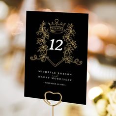 a black and gold wedding table number with a heart on it's stand in front of some flowers