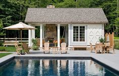 a pool house with chairs and an umbrella next to the swimming pool in front of it