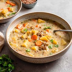 two bowls filled with soup on top of a table next to some bread and vegetables