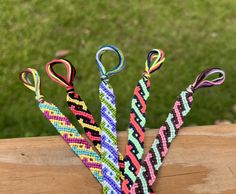 four colorful bracelets are tied together on a piece of wood in front of some grass