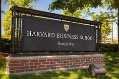 the harvard business school sign in front of a brick wall and grass area with trees