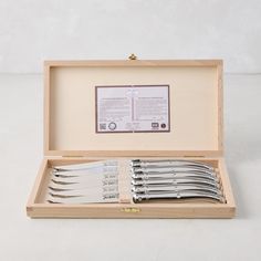 a set of silverware in a wooden box on a white surface with an information card