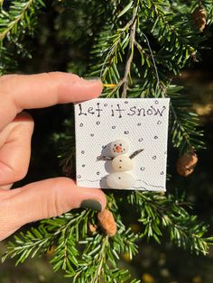 a hand holding a small christmas ornament with two snowmen on it