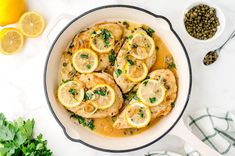 a pan filled with chicken and lemons next to some garnish on the side