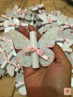 a hand holding a small white tube with pink bows on it and lots of paper flowers in the background