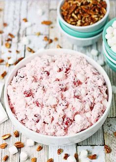 a bowl full of cherry pie salad with marshmallows and pecans in the background