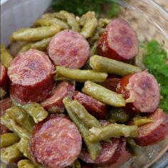 a glass bowl filled with green beans and sausage