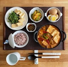 a wooden table topped with bowls and plates filled with different types of food next to utensils