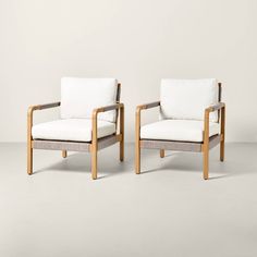 two wooden chairs with white cushions sitting next to each other on a gray flooring