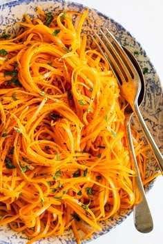 a blue and white bowl filled with spaghetti on top of a table next to a fork