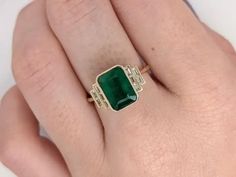 a woman's hand with a green ring on top of her finger and an emerald stone in the middle