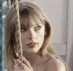 a woman with blonde hair holding onto a rope in front of her face and looking at the camera