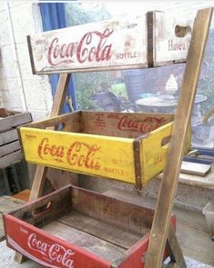 an old coca - cola crate is sitting on top of a wooden shelf with two soda cans in it