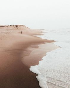 a person walking along the beach in front of an ocean shore line with sand and water