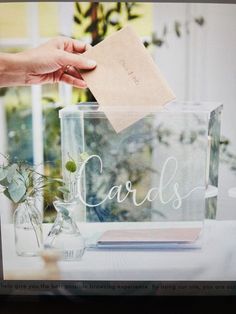 a person holding a piece of paper over a glass box that says cards on it