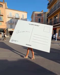 a woman holding up a large white sign in the middle of a street with buildings behind her