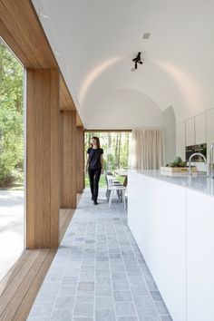 a woman walking down a long hallway between two white walls with windows on both sides