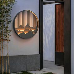 a round mirror on the side of a building next to a bamboo plant and potted tree