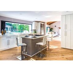 a large kitchen with an island in the middle and white cabinets on both sides, along with two bar stools