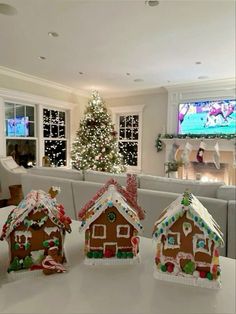 three gingerbread houses are sitting on a table in front of a christmas tree and television