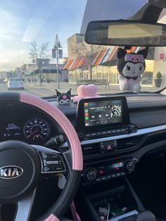 the interior of a car with pink steering wheel cover and plush animals on the dashboard