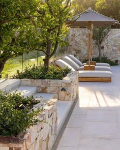 an outdoor patio with lounge chairs, trees and stone walls on either side of the pool