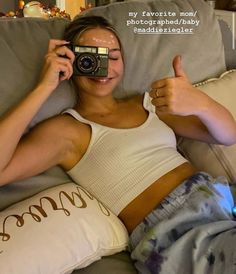 a woman laying on top of a couch holding a camera and giving the thumbs up