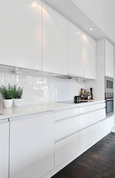 a kitchen with white cabinets and wooden floors is pictured in this image, there are plants on the counter