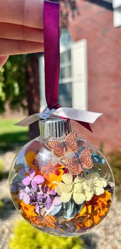 a hand holding a glass ornament filled with colorful flowers and butterfly shapes in front of a brick building