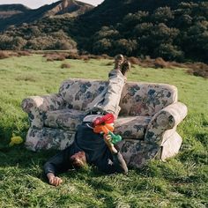 a man laying on top of a couch in a field next to a green hillside