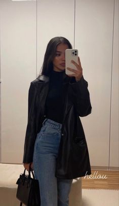 a woman taking a selfie in front of a mirror wearing jeans and a leather jacket