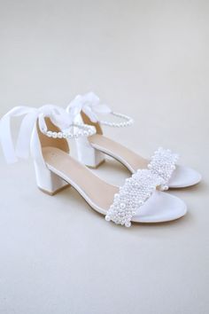 a pair of white wedding shoes with pearls on the toe and heel, tied together