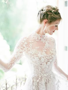 a woman in a wedding dress standing by a window with her hands on her hips