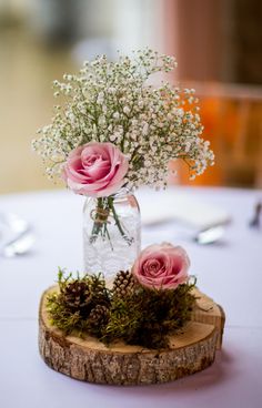 pink roses and baby's breath are in a mason jar on a wood slice