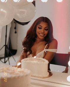 a woman sitting at a table with a cake in front of her and balloons behind her