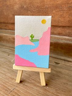 a small easel with a painting on it sitting on top of a wooden table