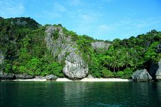 an island surrounded by lush green trees on the water's edge with rocks in the foreground