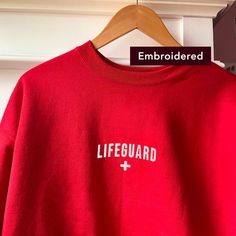 "\"Lifeguard\" embroidered on a comfy vintage-style crewneck. If you're on the lookout for both style and comfort, this fleece sweatshirt is the perfect choice. And with up to 5% recycled polyester in components, you'll be taking a little step closer to a more earth-friendly way of life. * Sizes are unisex * 50% cotton, 50% polyester (up to 5% recycled polyester, made from plastic bottles) * Fabric weight: 7.8 oz/y² (264.5 g/m²) * Patented low-pill, high-stitch density PrintPro® XP fleece * Doub Sporty Embroidered Crew Sweatshirt, Red Crew Neck Sweatshirt With Relaxed Fit, Red Relaxed Fit Crew Sweatshirt, Fleece Crew Neck Sweater With Letter Embroidery, Casual Crew Sweatshirt With Embroidered Graphics, Long Sleeve French Terry Sweatshirt With Embroidered Logo, Oversized College Sweatshirt With Embroidered Graphics, Oversized Embroidered College Sweatshirt, Casual Oversized Sweater With Embroidered Logo