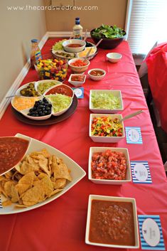 a red table topped with plates of food and bowls filled with salsa, guacamole, tortilla chips